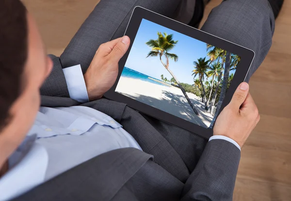 Businessman Looking At Beach Photo On Tablet