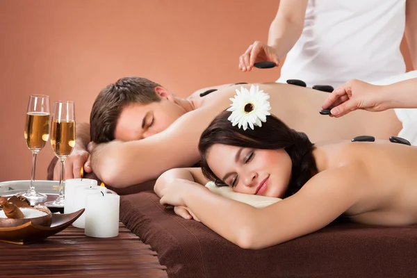 Relaxed Couple Receiving Hot Stone Therapy At Spa