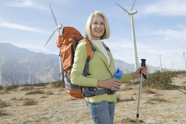 Senior Woman With Hiking Pole And Backpack At Windfarm