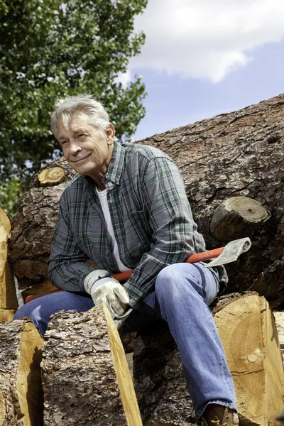 Senior man sitting on wood logs with an axe
