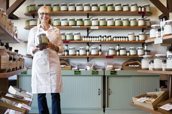 Portrait of a happy senior merchant standing with spice jar in store