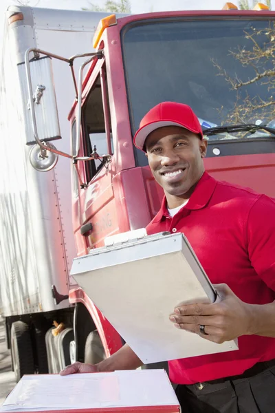 Portrait of a happy African American man holding clipboard with delivery truck in background