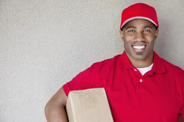 Portrait of a African American delivery man holding package against wall