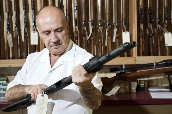 Mature gun shop merchant looking at rifle in store