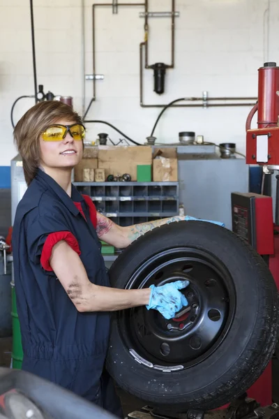 Portrait of a confident young female mechanic carrying tire in vehicle repair shop