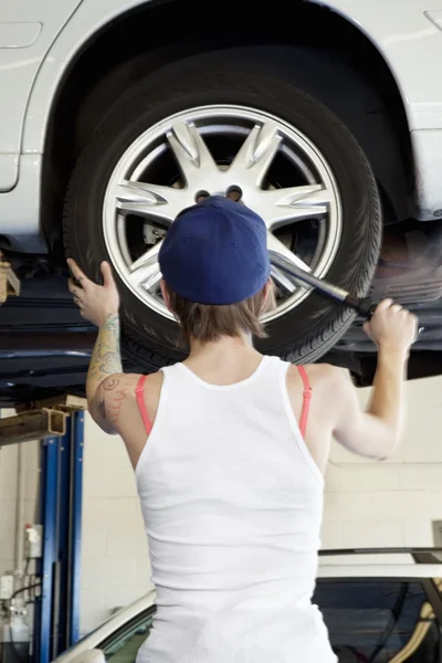 Back view of young female mechanic working on lifted car\'s tire in automobile repair shop