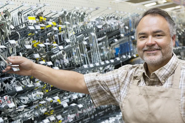 Portrait of a happy mature salesperson holding metallic equipment in hardware store