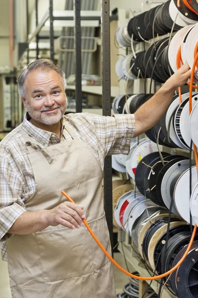 Portrait of a happy mature store clerk with electrical wire spool in hardware shop