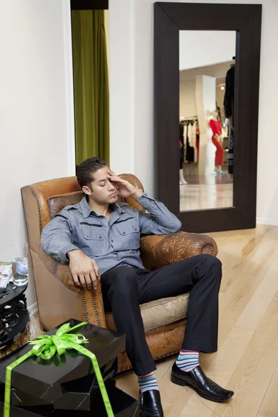 Tired young man sitting on armchair in fashion store