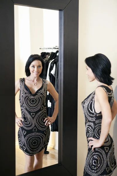 Happy mid adult woman wearing a stylish dress standing in front of mirror with hands on hips in boutique