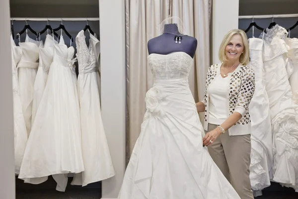 Portrait of a happy senior female adjusting wedding dress on mannequin in bridal store