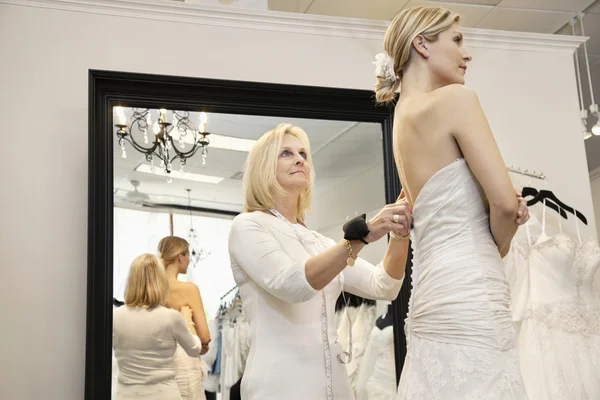 Senior owner assisting young bride getting dressed in wedding gown — Stock Photo #21883347
