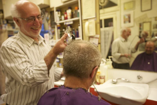 Happy man cutting senior customer\'s hair with razor