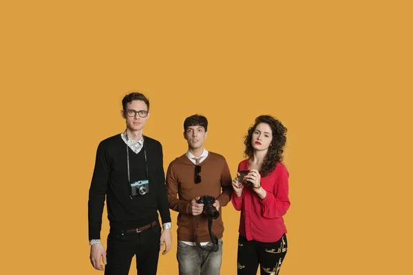 Portrait of friends standing together with cameras over colored background