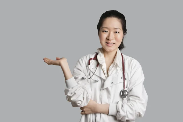 Portrait of an Asian female doctor displaying an invisible product over gray background