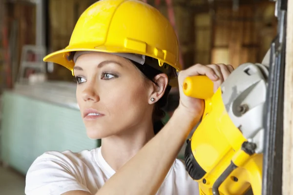 Female construction worker cutting wood with a power saw while looking away