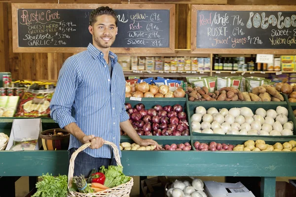 Handsome young man holding basket at vegetable stall in supermarket