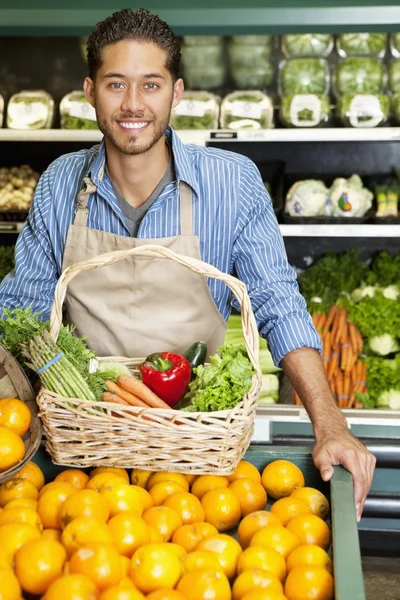 Portrait of a happy man with vegetable basket standing near oranges stall in supermarket