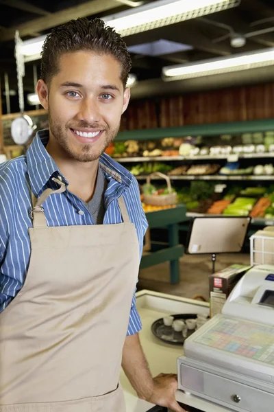 Portrait of handsome store employee standing near cash register in supermarket