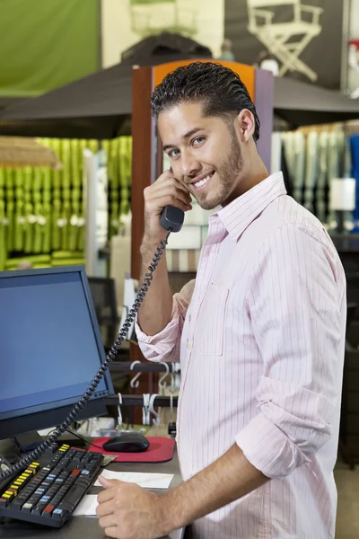 Portrait of a happy salesperson listening to telephone receiver in store