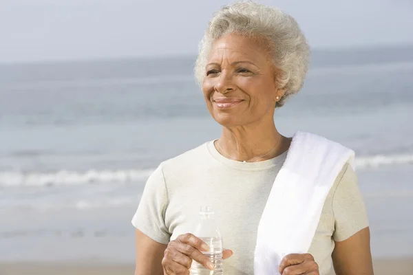 Senior Woman Holding Bottle And Towel At Beach