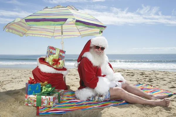 Santa Claus Sitting Under Parasol With Gifts On Beach