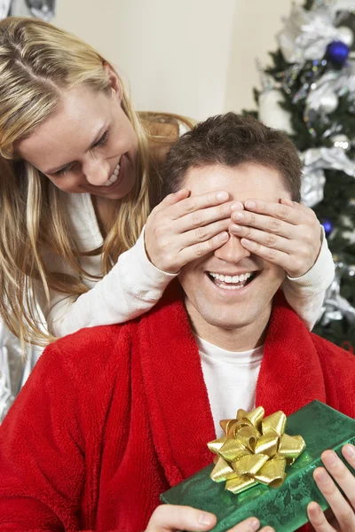 Woman Covering Eyes Of Man Holding Present
