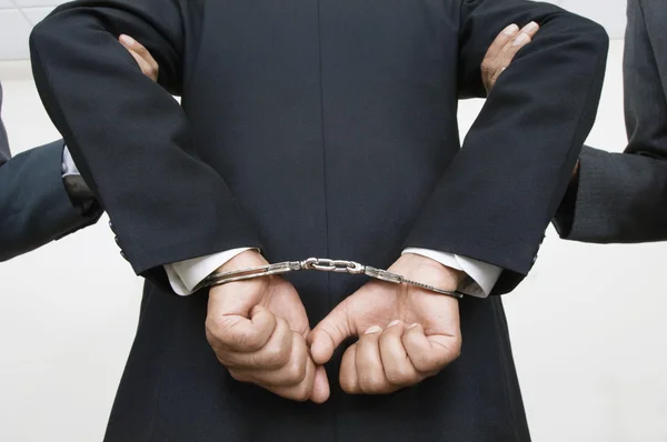 Businessman With Handcuffs While Partners Holding His Arms