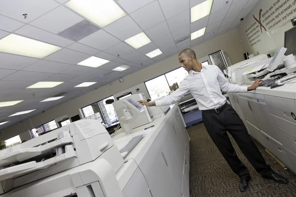 Man working in printing press between two cash register machine