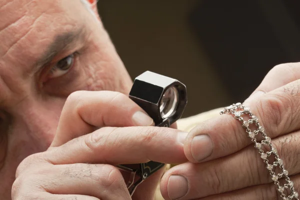Close up of man looking at jewelry through magnifying glass
