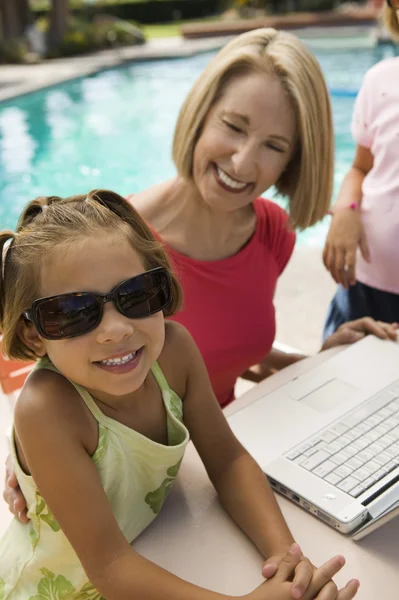 Girls using laptop with grandmother by swimming pool