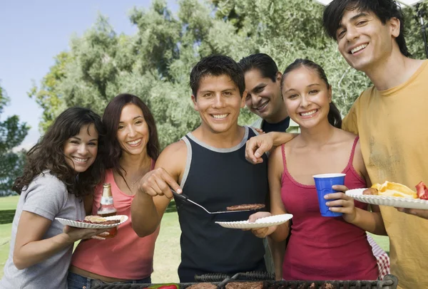 People gathered around grill at outdoor picnic.