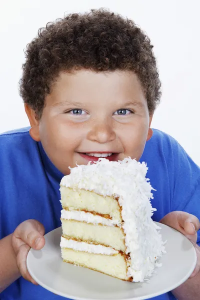 Overweight boy holding large slice of cake