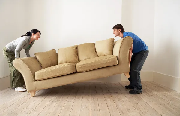 Couple lifting sofa in empty room