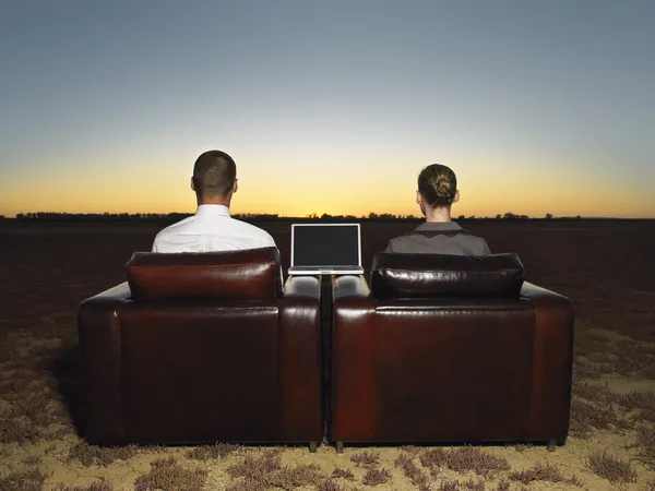 Business people sitting in armchairs in open plain