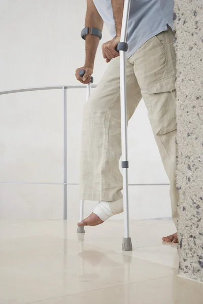 Injured man with wrapped ankle on crutches