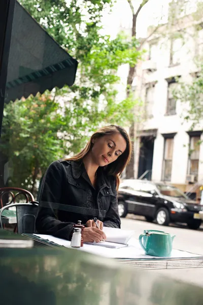 Woman writing at sidewalk cafe