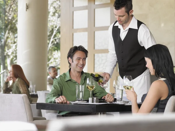 Waiter pouring wine for couple at restaurant