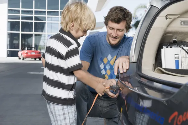 Father and son attaching electrical plug to electric car