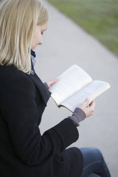 Blonde woman sits reading book outside on path