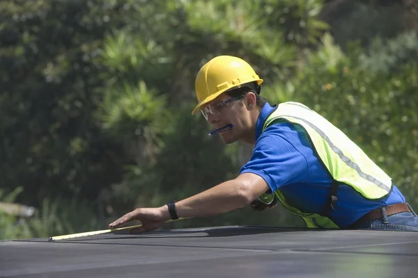 Maintenance worker measures solar array on rooftop