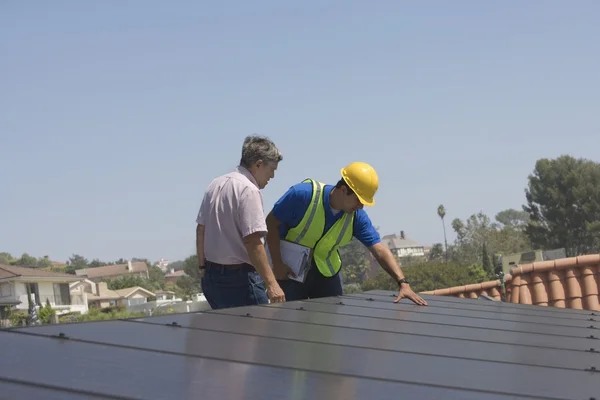Maintenance workers stand with solar array on rooftop