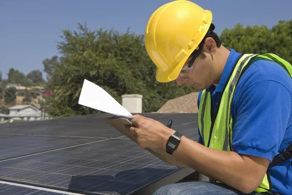 Maintenance worker makes notes with solar array on rooftop