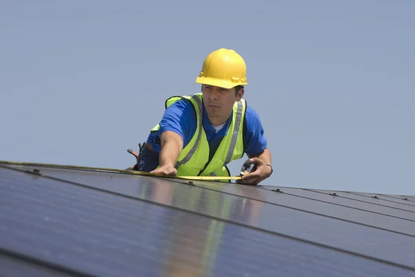 Maintenance worker measures solar array on rooftop