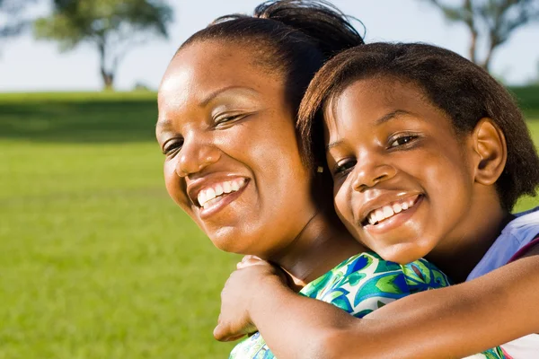 Happy african american mother and daughter piggyback outdoors