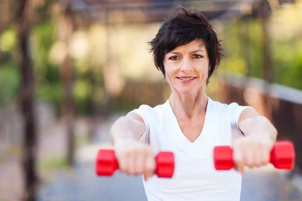 Happy middle aged woman exercise with dumbbells outdoors