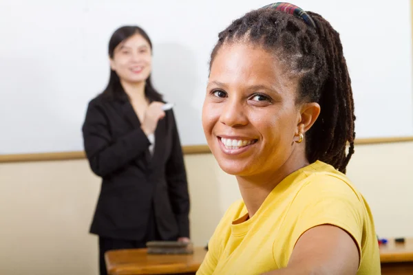 Adult african student in classroom, background is a teacher standing in front of white board