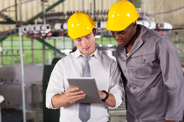 Factory manager and worker looking at tablet computer