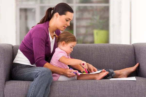 Mother teaching daughter drawing on sofa at home