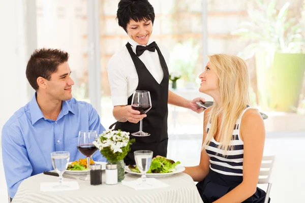 Waitress serving wine to diners in modern restaurant